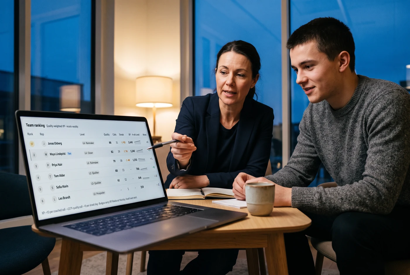 A sales manager pointing at a laptop that shows the DealPrompt team ranking, with a rep looking on
